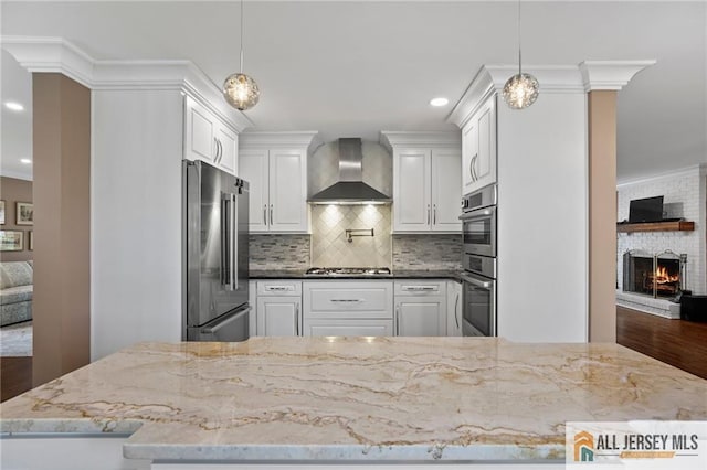 kitchen with stainless steel appliances, wall chimney range hood, white cabinets, decorative backsplash, and dark stone countertops