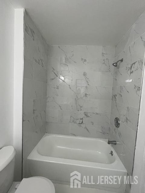 bathroom with tiled shower / bath combo and toilet