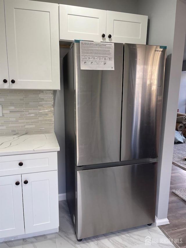 kitchen featuring light stone counters, stainless steel fridge, tasteful backsplash, and white cabinets