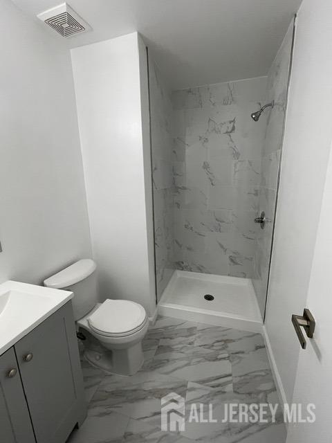 bathroom with vanity, toilet, and tiled shower