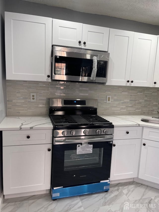 kitchen featuring stainless steel appliances, white cabinetry, light stone countertops, and backsplash