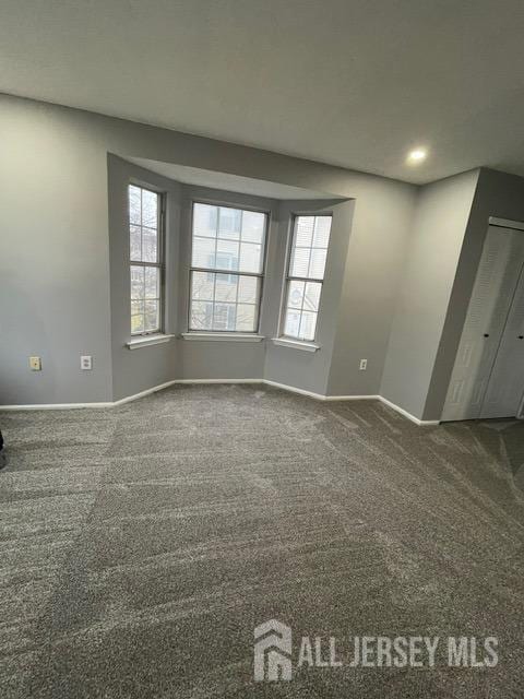 spare room featuring dark colored carpet and a wealth of natural light