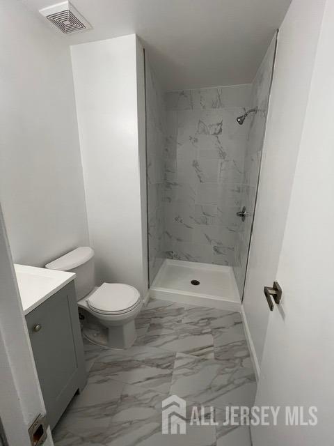 bathroom with vanity, tiled shower, and toilet