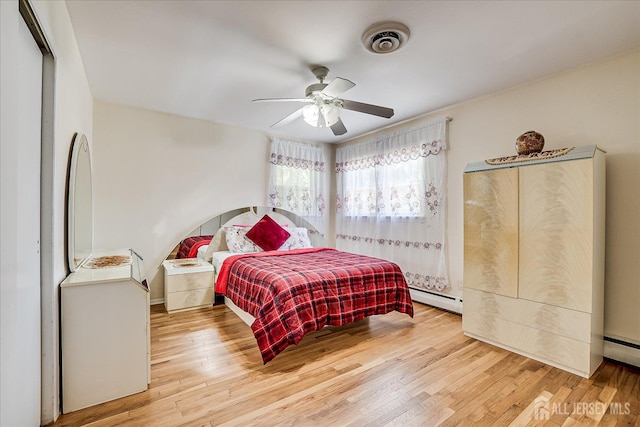 bedroom featuring a baseboard heating unit, wood finished floors, and ceiling fan