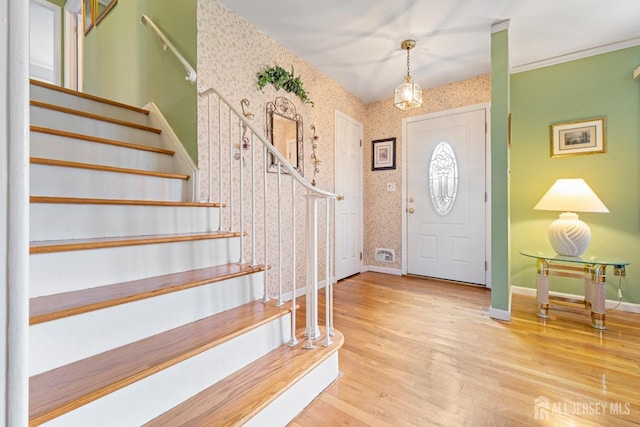 foyer entrance featuring wallpapered walls, stairs, baseboards, and wood finished floors