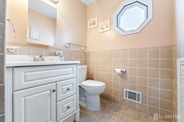 half bathroom with tile walls, vanity, toilet, tile patterned flooring, and wainscoting