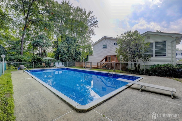 view of swimming pool featuring a wooden deck, fence, a diving board, and a patio