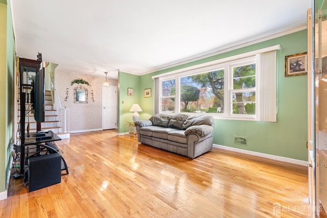 living room with baseboards, wallpapered walls, wood finished floors, stairs, and crown molding