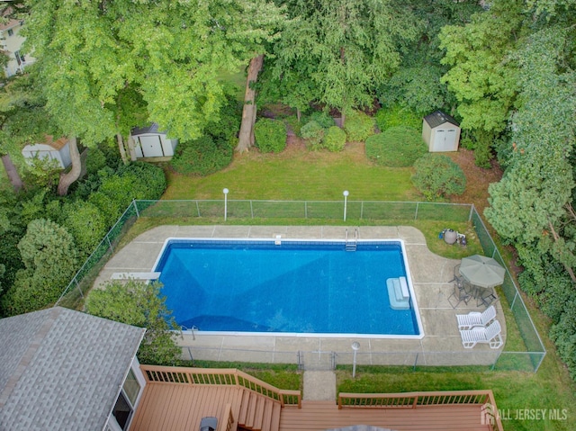 view of swimming pool featuring a storage unit, fence, an outdoor structure, and a deck