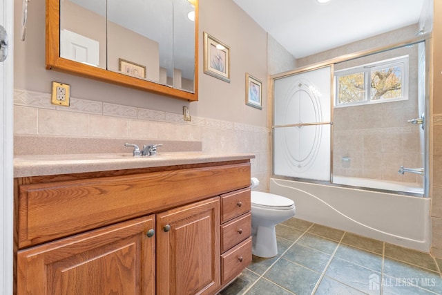 full bathroom featuring tile walls, toilet, vanity, tile patterned flooring, and shower / bath combination with glass door