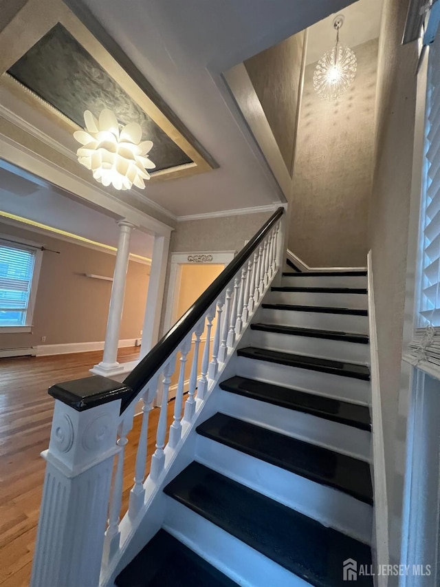 staircase featuring hardwood / wood-style floors, crown molding, a notable chandelier, and ornate columns