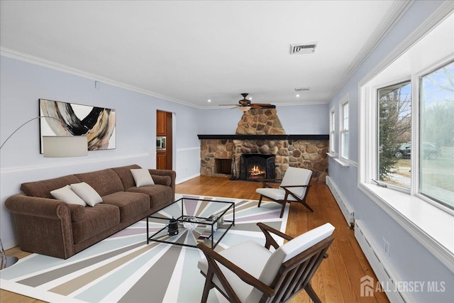 living room featuring visible vents, wood finished floors, crown molding, a stone fireplace, and a baseboard heating unit