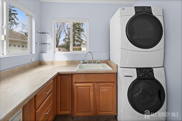 washroom with stacked washer and dryer, cabinet space, a wealth of natural light, and a sink