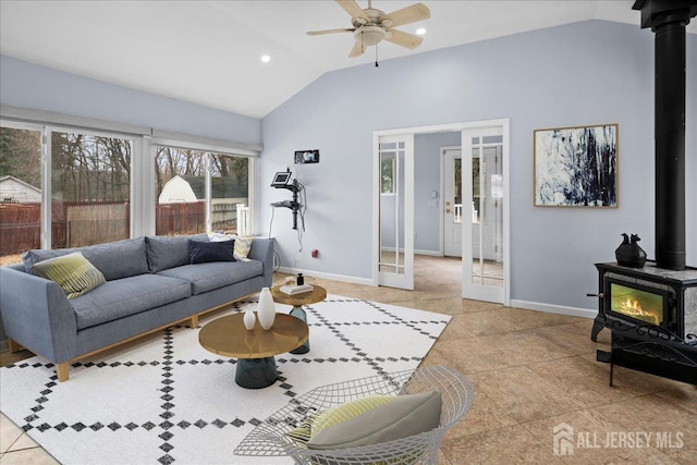 living room featuring lofted ceiling, a ceiling fan, a wood stove, and baseboards