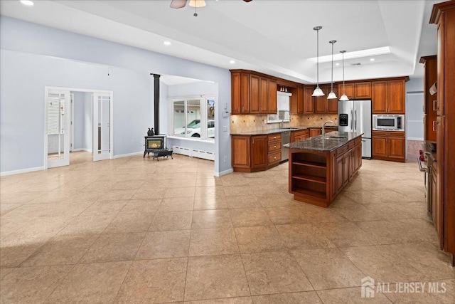 kitchen with a center island with sink, open shelves, a raised ceiling, hanging light fixtures, and appliances with stainless steel finishes