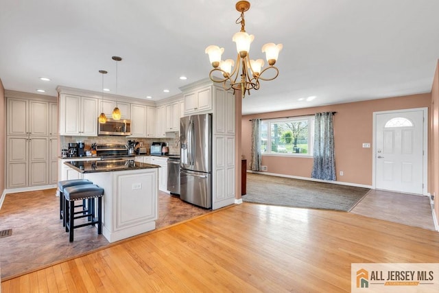 kitchen featuring a kitchen island, dark countertops, a chandelier, light wood-style flooring, and appliances with stainless steel finishes