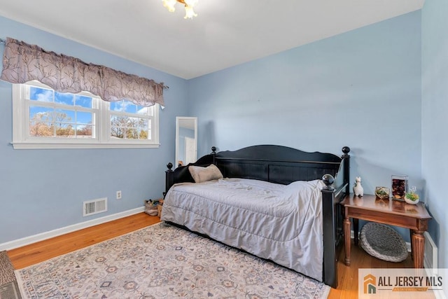 bedroom with baseboards, wood finished floors, and visible vents
