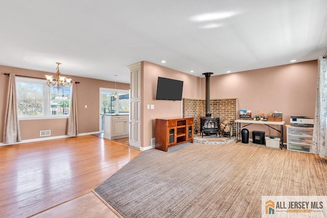 interior space with visible vents, a wood stove, baseboards, a chandelier, and light wood-style flooring