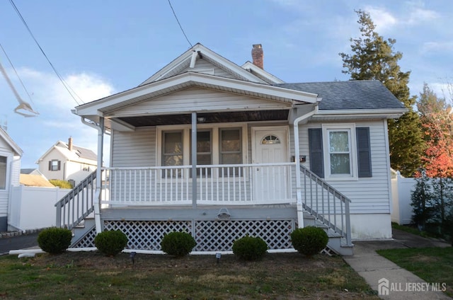 bungalow-style house with covered porch, roof with shingles, fence, and a chimney