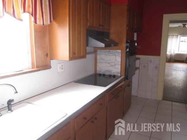 458 S Barclay St, Perth Amboy, NJ 08861 - kitchen featuring wall chimney exhaust hood, black electric stovetop, wall oven, light tile patterned floors, and light countertops
