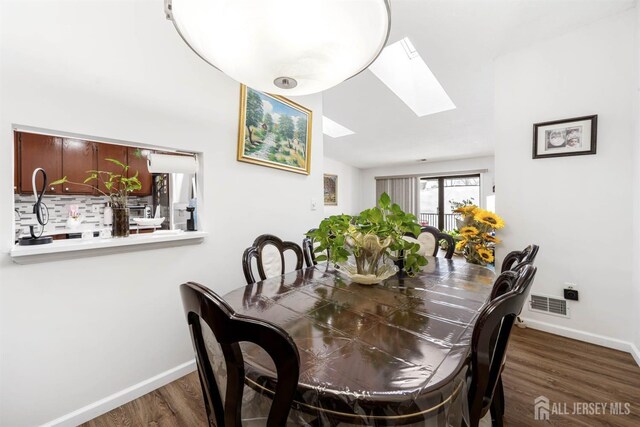 dining space featuring vaulted ceiling with skylight, dark wood-style flooring, visible vents, and baseboards