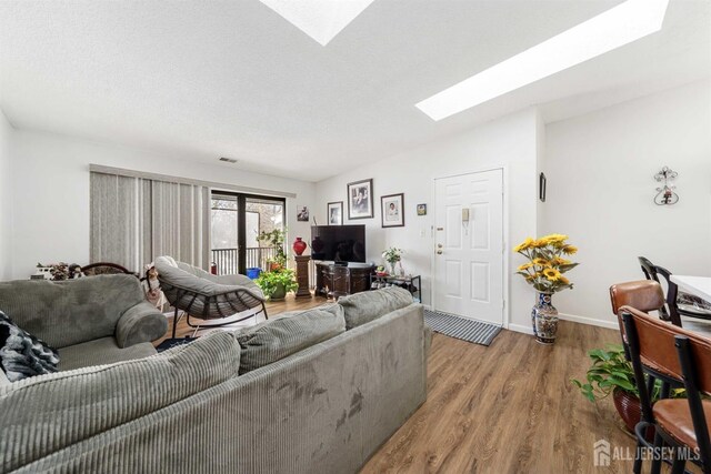 living room with a skylight, light wood finished floors, baseboards, visible vents, and a textured ceiling