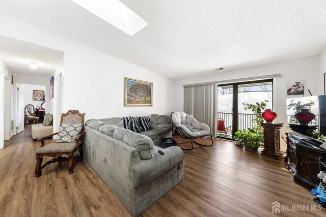 living area featuring lofted ceiling with skylight, dark wood-style flooring, and visible vents