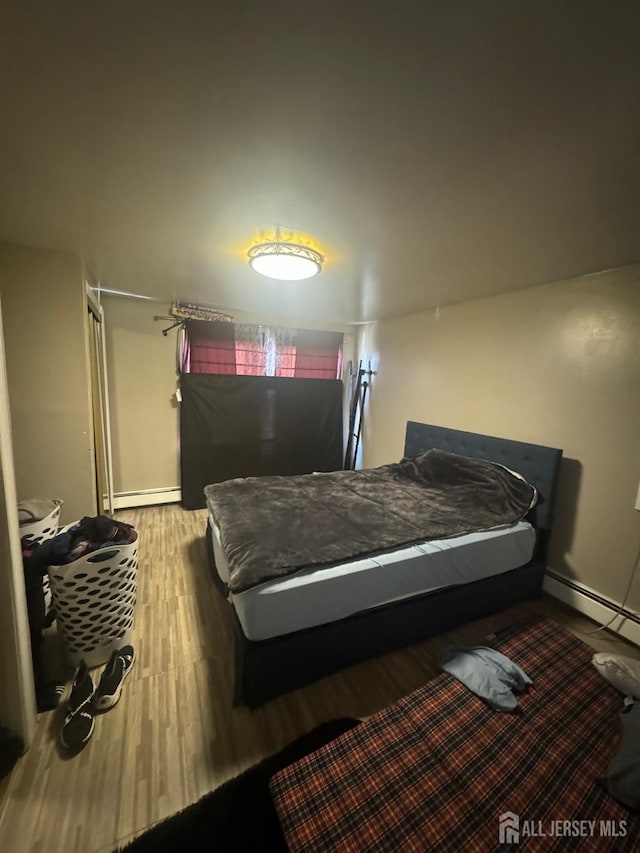 bedroom with hardwood / wood-style floors and a baseboard heating unit