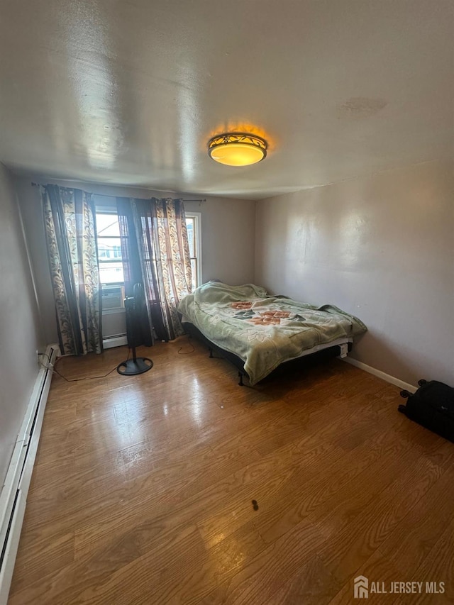 unfurnished bedroom with wood-type flooring and baseboard heating