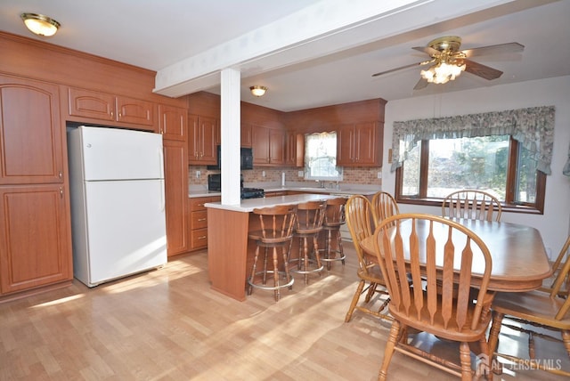 kitchen with light wood finished floors, light countertops, decorative backsplash, freestanding refrigerator, and beamed ceiling