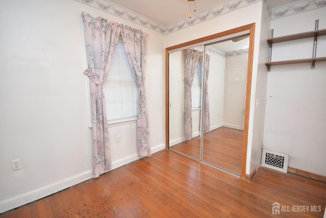 unfurnished bedroom featuring baseboards, a closet, visible vents, and hardwood / wood-style floors