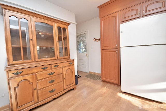 kitchen with light wood-style floors, baseboards, glass insert cabinets, and freestanding refrigerator