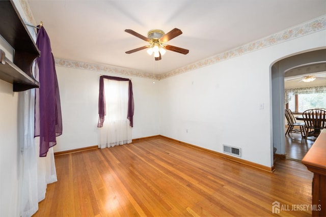 spare room with arched walkways, ceiling fan, light wood-type flooring, and visible vents