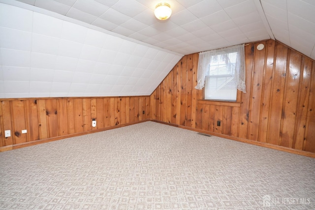 bonus room featuring carpet floors, wood walls, visible vents, baseboards, and vaulted ceiling