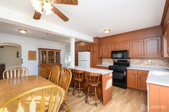 kitchen featuring arched walkways, decorative backsplash, light countertops, black appliances, and a sink