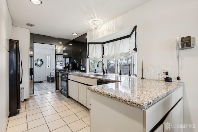 kitchen with a sink, white cabinets, black appliances, light tile patterned floors, and a peninsula