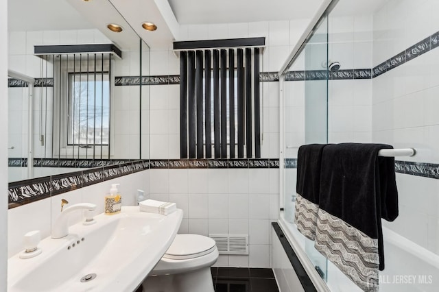 bathroom featuring tile walls, tiled shower, toilet, tile patterned flooring, and a sink