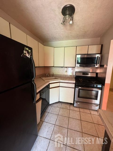 165 Penn Ct, Old Bridge, NJ 07747 - kitchen with black appliances, a sink, a textured ceiling, tile countertops, and light tile patterned flooring