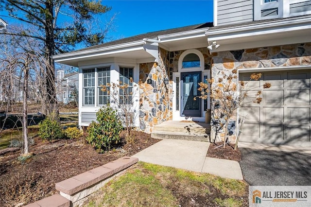 view of exterior entry with a garage, stone siding, and driveway