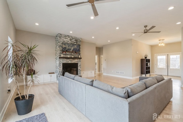 living room with ceiling fan with notable chandelier, a fireplace, and light wood-type flooring