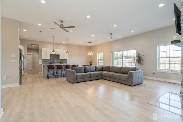 living room with sink, ceiling fan with notable chandelier, and light hardwood / wood-style flooring