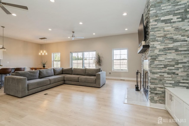 living room with a stone fireplace, ceiling fan with notable chandelier, and light hardwood / wood-style flooring