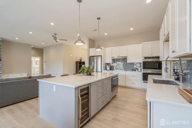 kitchen featuring appliances with stainless steel finishes, pendant lighting, white cabinetry, beverage cooler, and a center island