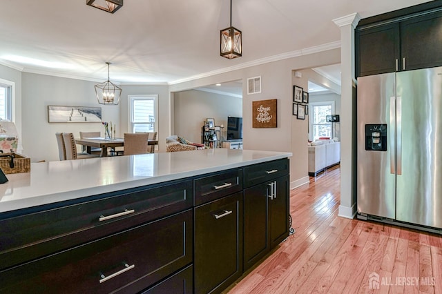 kitchen featuring stainless steel fridge, crown molding, light countertops, hanging light fixtures, and healthy amount of natural light