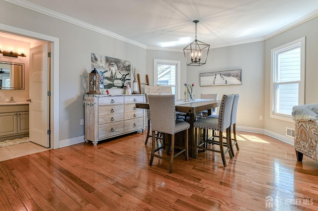 dining area with a chandelier, light wood-style flooring, crown molding, and baseboards