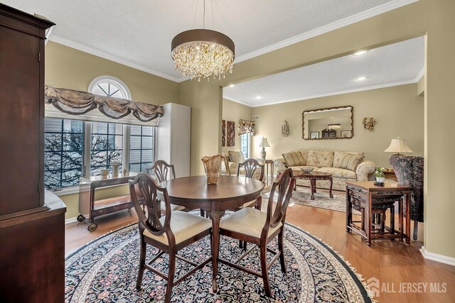 dining room with a textured ceiling, ornamental molding, a notable chandelier, and light hardwood / wood-style flooring