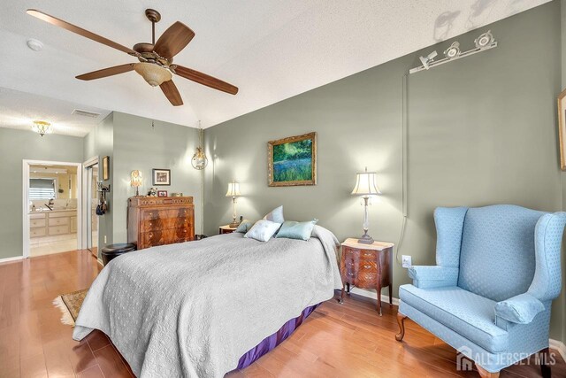 bedroom with a textured ceiling, vaulted ceiling, hardwood / wood-style floors, ceiling fan, and ensuite bath