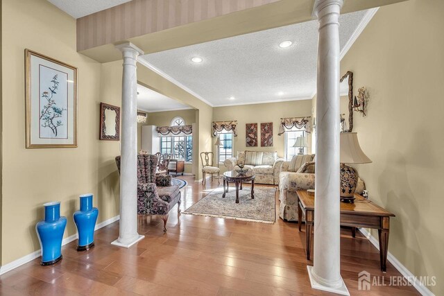 living room featuring decorative columns, a textured ceiling, ornamental molding, and hardwood / wood-style flooring