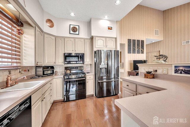 kitchen featuring sink, a textured ceiling, light hardwood / wood-style flooring, backsplash, and appliances with stainless steel finishes