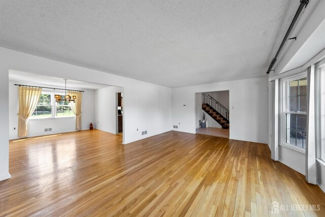 85 Hidden Lake Dr, North Brunswick, NJ 08902 - unfurnished living room with light wood-style flooring, a chandelier, a textured ceiling, and stairway